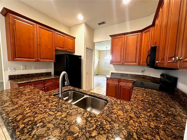 kitchen featuring dark stone countertops, light tile patterned floors, black appliances, kitchen peninsula, and sink