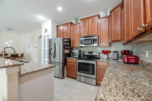 kitchen with arched walkways, stainless steel appliances, backsplash, light stone countertops, and pendant lighting