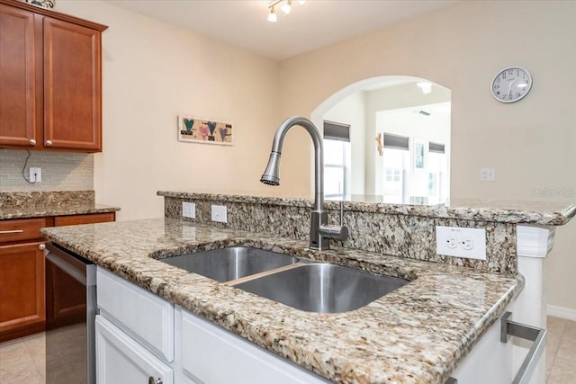 kitchen with light tile patterned flooring, light stone countertops, a sink, stainless steel dishwasher, and decorative backsplash