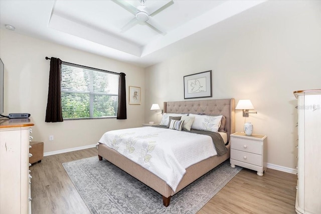 bedroom with light wood-type flooring, baseboards, a tray ceiling, and ceiling fan