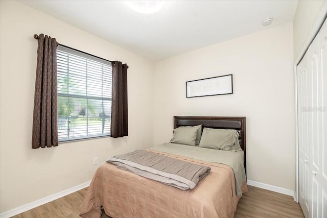 bedroom with light wood finished floors, a closet, and baseboards