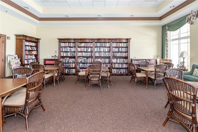 living area with a tray ceiling, wall of books, and carpet