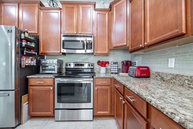 kitchen with appliances with stainless steel finishes, decorative backsplash, light stone counters, and light tile patterned floors