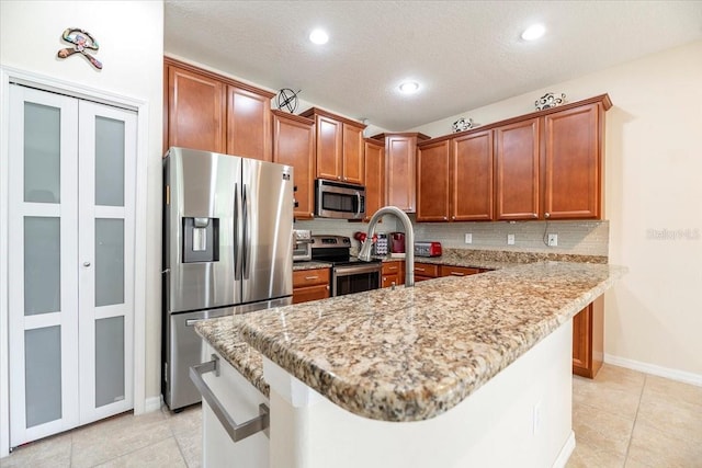 kitchen with brown cabinetry, a breakfast bar area, light stone countertops, stainless steel appliances, and backsplash