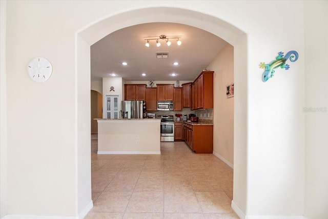 kitchen with arched walkways, a center island, brown cabinets, visible vents, and appliances with stainless steel finishes