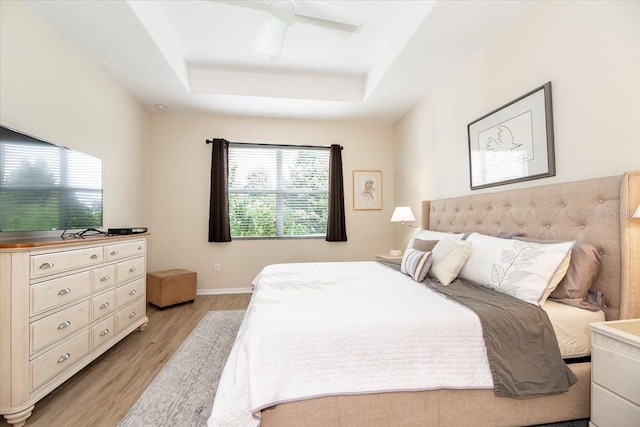 bedroom with light wood-type flooring, a raised ceiling, ceiling fan, and baseboards