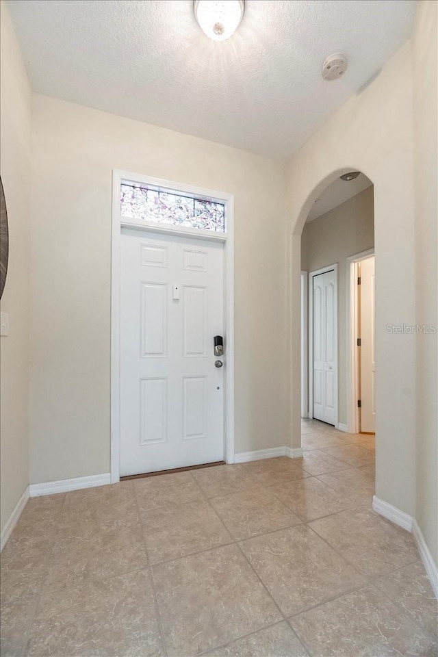 entryway featuring baseboards, arched walkways, and a textured ceiling