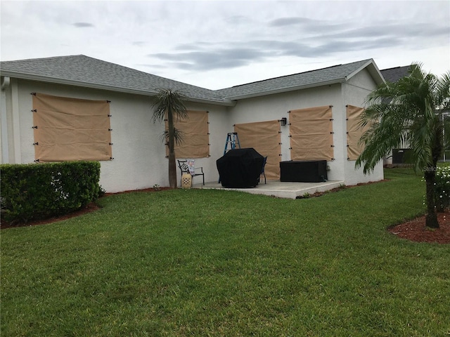 back of house with a shingled roof, a patio, a lawn, and stucco siding