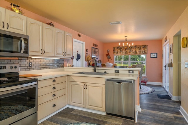 kitchen with sink, kitchen peninsula, an inviting chandelier, appliances with stainless steel finishes, and dark hardwood / wood-style flooring