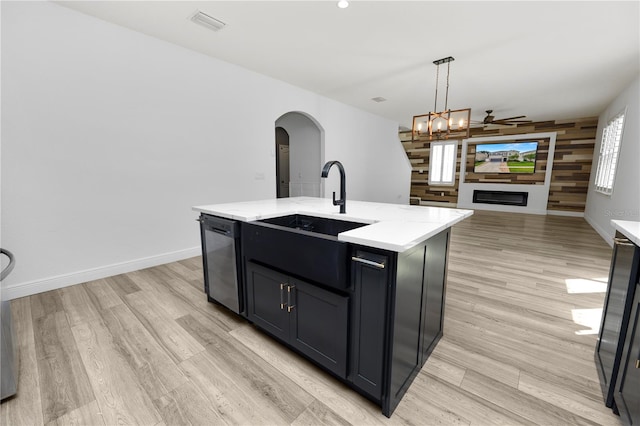 kitchen with ceiling fan with notable chandelier, wooden walls, decorative light fixtures, stainless steel dishwasher, and a center island with sink