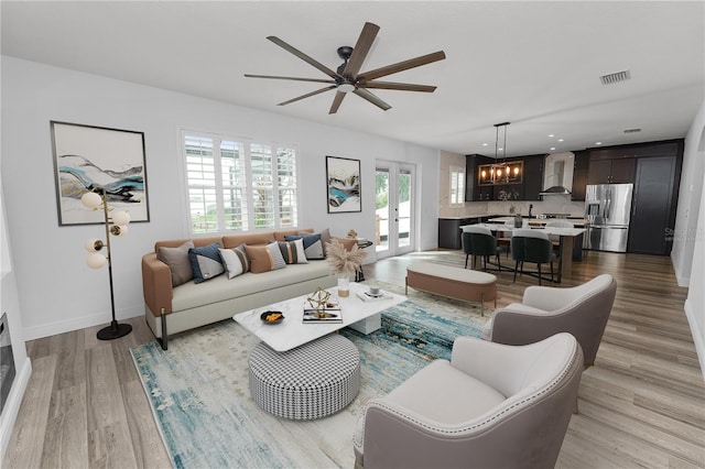 living room with french doors, ceiling fan with notable chandelier, and light wood-type flooring