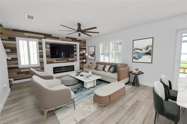 living room with ceiling fan, light hardwood / wood-style floors, and wood walls