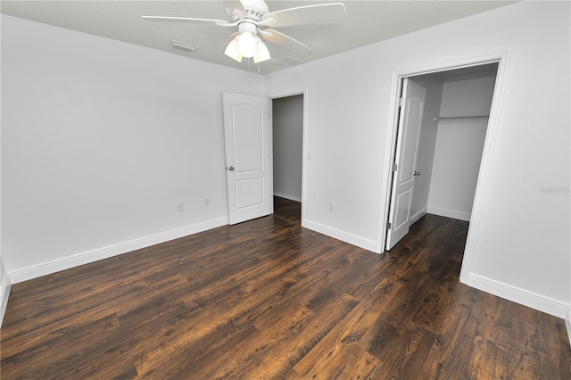 unfurnished bedroom with ceiling fan, a spacious closet, dark hardwood / wood-style flooring, and a closet