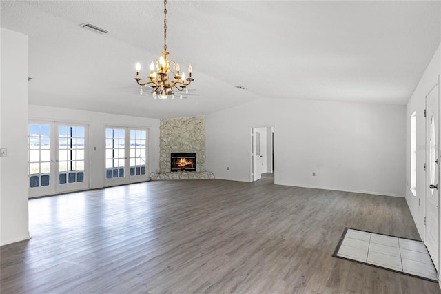 unfurnished living room featuring wood-type flooring, a stone fireplace, vaulted ceiling, french doors, and a chandelier