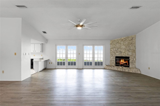 unfurnished living room featuring wood-type flooring, a stone fireplace, and a textured ceiling