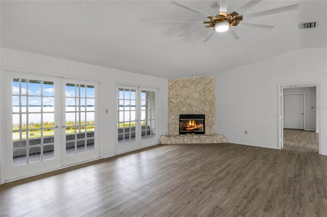 unfurnished living room featuring lofted ceiling, hardwood / wood-style flooring, a textured ceiling, a stone fireplace, and french doors