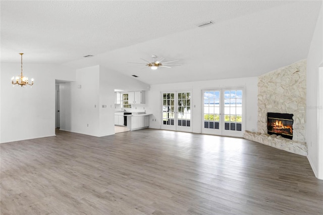 unfurnished living room with hardwood / wood-style flooring, a stone fireplace, ceiling fan with notable chandelier, and a textured ceiling