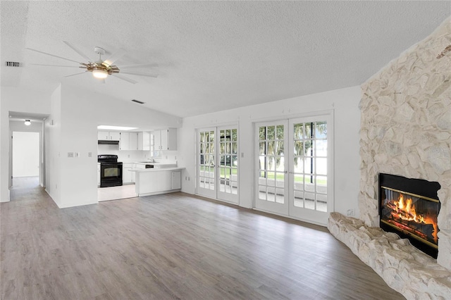 unfurnished living room with a stone fireplace, vaulted ceiling, a textured ceiling, and hardwood / wood-style flooring