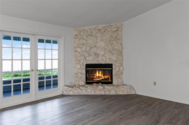 unfurnished living room with french doors, a stone fireplace, hardwood / wood-style floors, and a textured ceiling