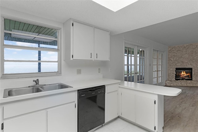 kitchen with a stone fireplace, a wealth of natural light, white cabinetry, dishwasher, and sink