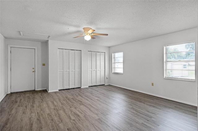 unfurnished bedroom with two closets, a textured ceiling, ceiling fan, and hardwood / wood-style flooring