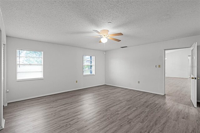 unfurnished room with ceiling fan, plenty of natural light, dark wood-type flooring, and a textured ceiling