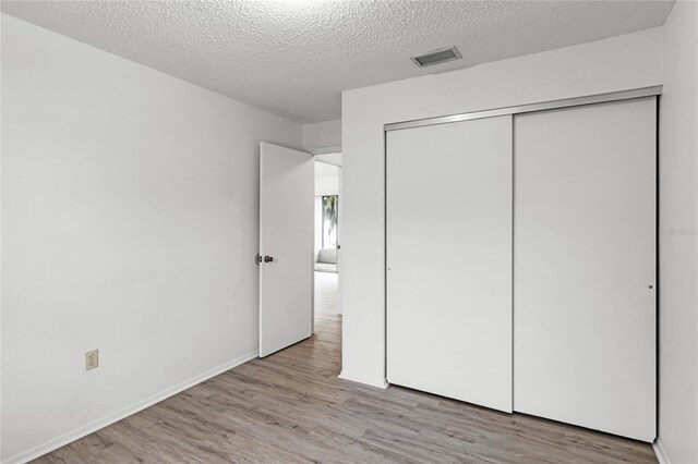 unfurnished bedroom featuring a closet, a textured ceiling, and light wood-type flooring