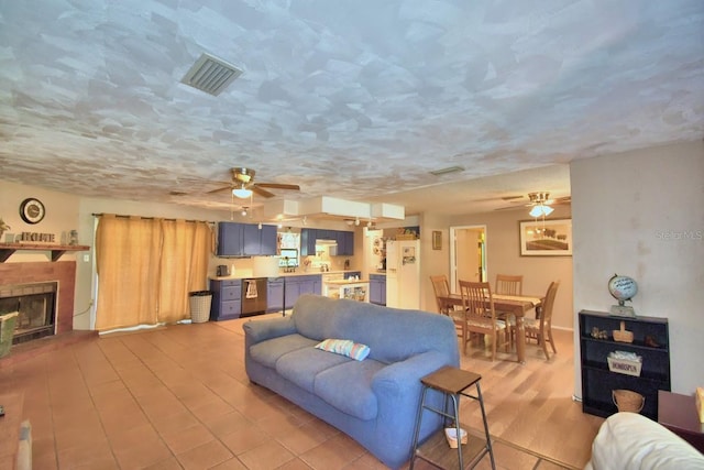 living room with light wood-type flooring, ceiling fan, a textured ceiling, and a fireplace