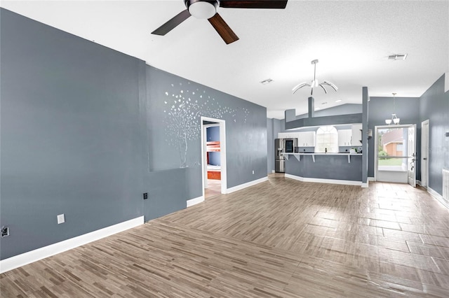 unfurnished living room featuring ceiling fan with notable chandelier, vaulted ceiling, a textured ceiling, and hardwood / wood-style floors