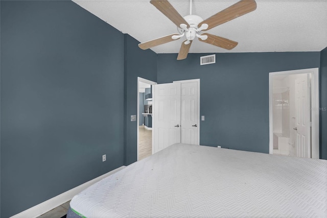 bedroom with a textured ceiling, vaulted ceiling, connected bathroom, hardwood / wood-style floors, and ceiling fan