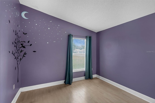 empty room with a textured ceiling, vaulted ceiling, and light hardwood / wood-style flooring