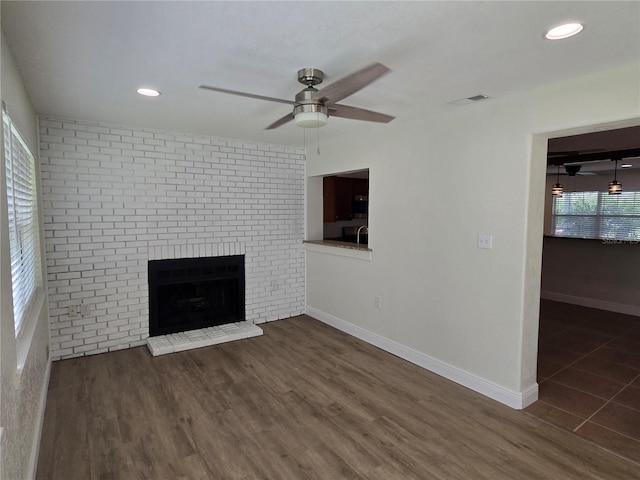 unfurnished living room featuring a fireplace, ceiling fan, dark hardwood / wood-style floors, and a healthy amount of sunlight