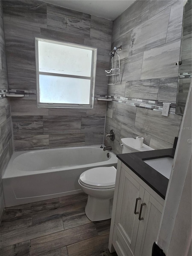 full bathroom with tile walls, hardwood / wood-style flooring, vanity, tiled shower / bath, and toilet