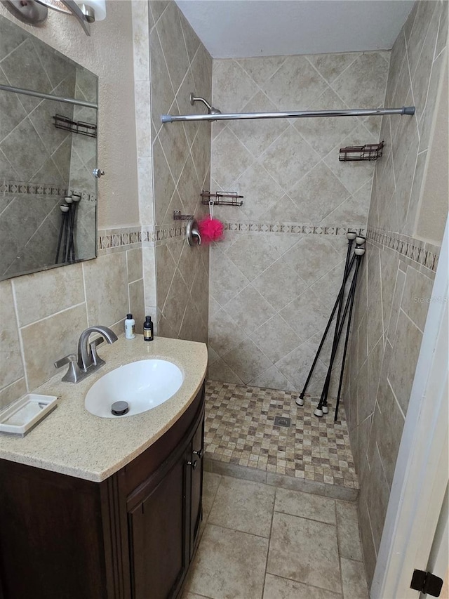 bathroom with a tile shower, vanity, tile walls, and tile patterned floors