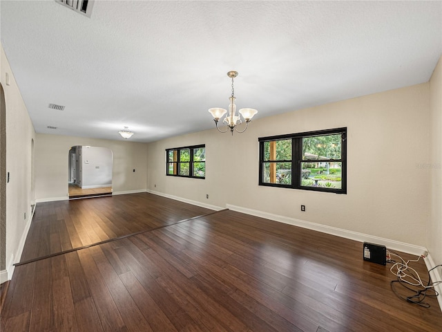 empty room featuring a chandelier, a textured ceiling, and dark hardwood / wood-style flooring