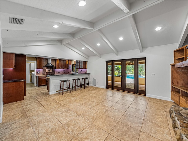 kitchen with a breakfast bar area, kitchen peninsula, wall chimney exhaust hood, vaulted ceiling with beams, and backsplash