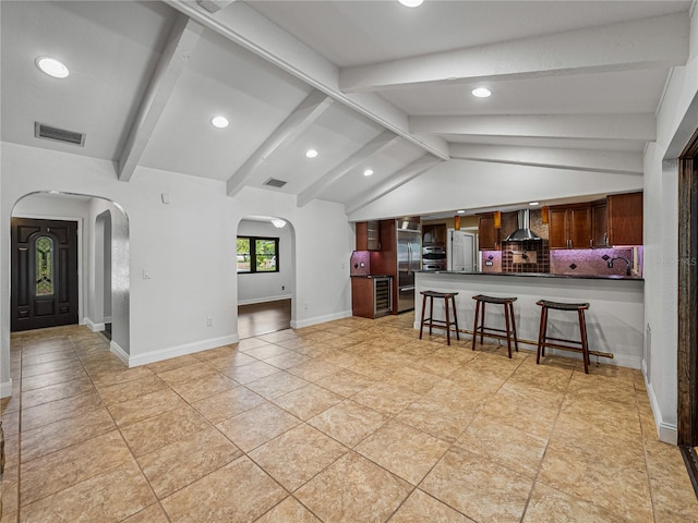 kitchen with vaulted ceiling with beams, kitchen peninsula, wall chimney exhaust hood, built in fridge, and a kitchen breakfast bar