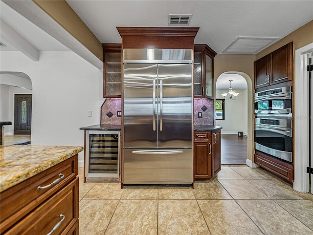 kitchen with dark stone counters, beverage cooler, decorative backsplash, appliances with stainless steel finishes, and light tile patterned floors