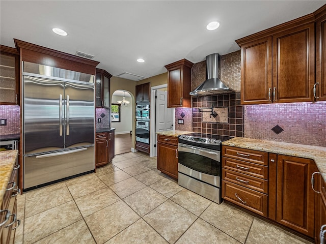 kitchen featuring light tile patterned flooring, appliances with stainless steel finishes, tasteful backsplash, and wall chimney range hood