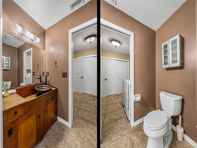 bathroom featuring a textured ceiling, washer and clothes dryer, vanity, and toilet