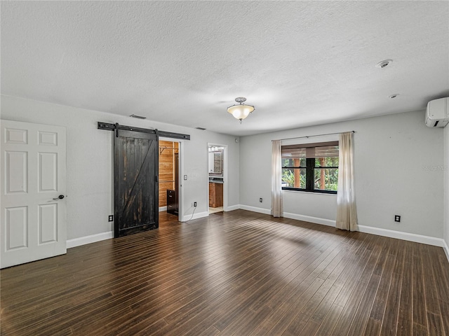 unfurnished living room featuring a barn door, a textured ceiling, an AC wall unit, and dark wood-type flooring