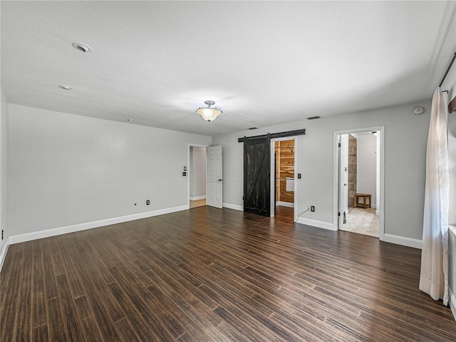 unfurnished room with a barn door, a textured ceiling, and dark wood-type flooring