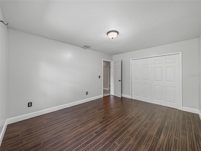 unfurnished bedroom featuring a textured ceiling, a closet, and dark wood-type flooring