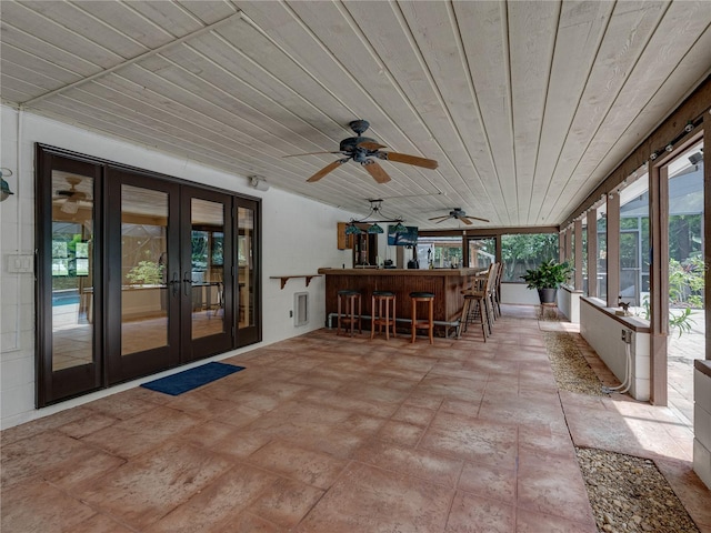 unfurnished sunroom featuring a healthy amount of sunlight, bar area, ceiling fan, and french doors