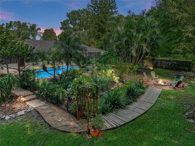 yard at dusk featuring glass enclosure, a fenced in pool, and an outdoor fire pit