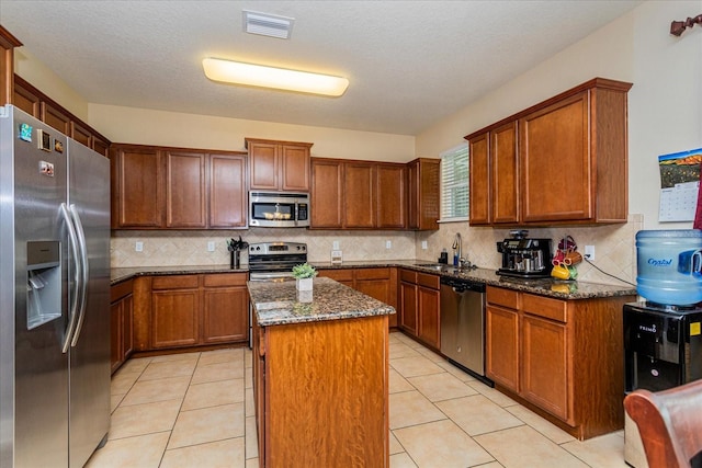 kitchen featuring appliances with stainless steel finishes, a textured ceiling, a center island, dark stone counters, and sink