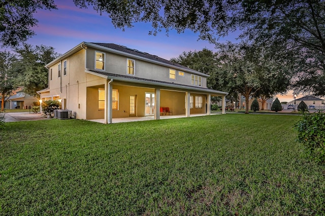 back house at dusk with a lawn, a garage, central AC unit, and a patio area