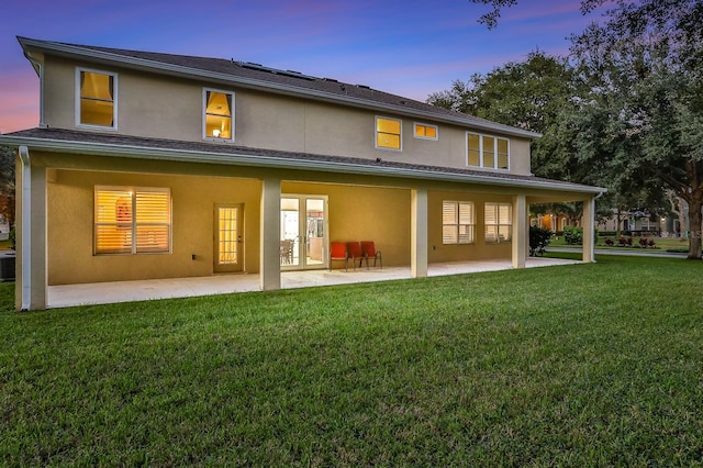 back house at dusk with a patio area, central air condition unit, and a yard