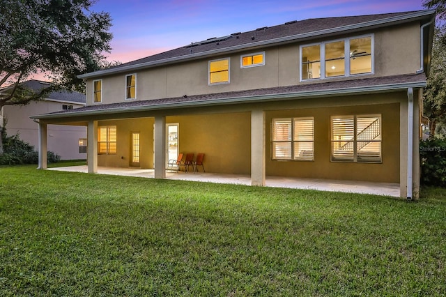 back house at dusk featuring a yard and a patio area