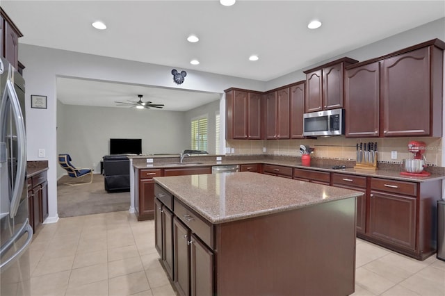 kitchen featuring stainless steel appliances, light stone counters, ceiling fan, and a kitchen island